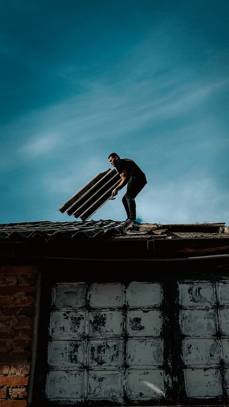 A roofer carrying a bundle of shingles across a rooftop